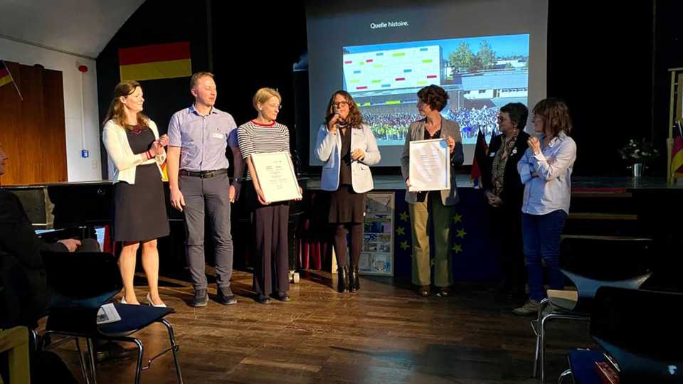 Die Urkunde für 50 Jahre Austausch wird von Evelyn Futterknecht an GAG- und Collège-Lehrkräfte überreicht.